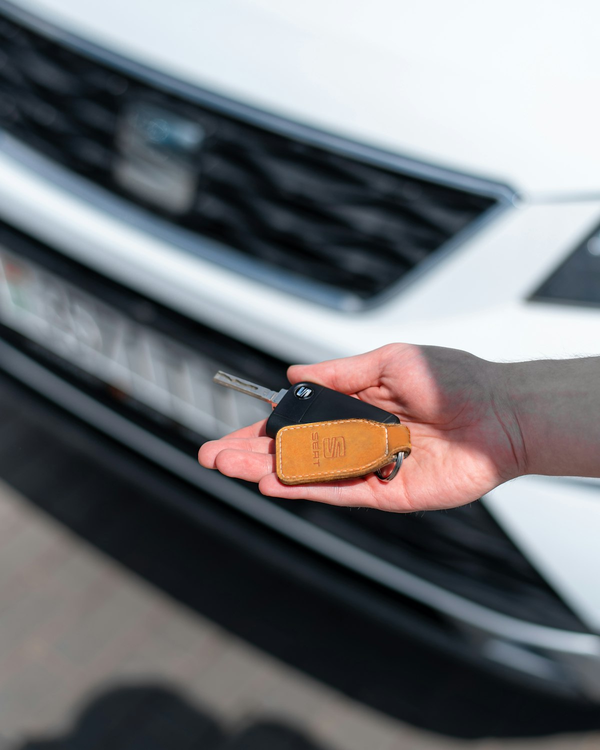 Hand holding a car key in front of a new white car