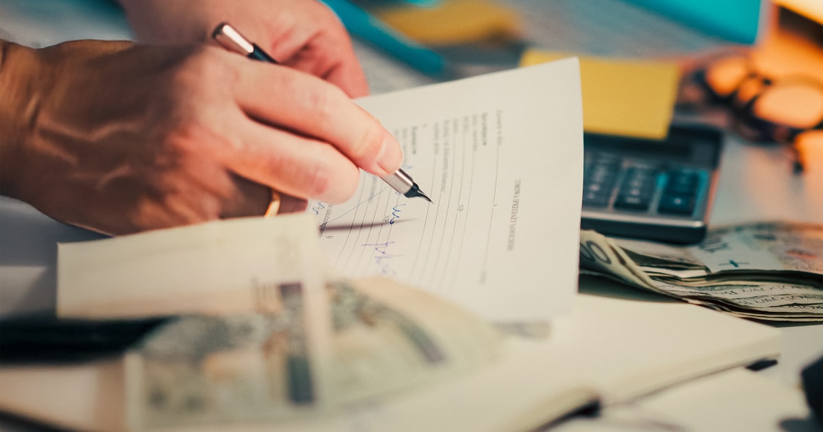 Hands signing loan paperwork with cash and a calculator